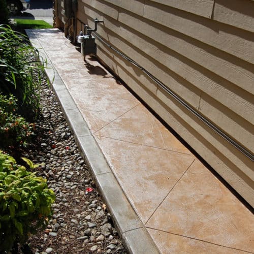 Colored concrete walkway runs down the side of a home