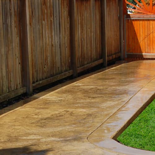 Colored stamped concrete walkway surrounded by grass and fence