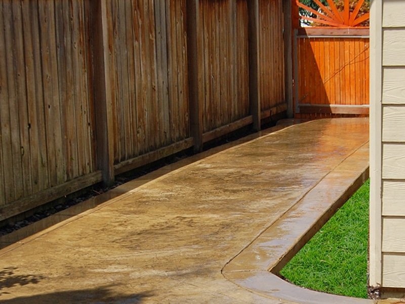 Colored stamped concrete walkway surrounded by grass and fence