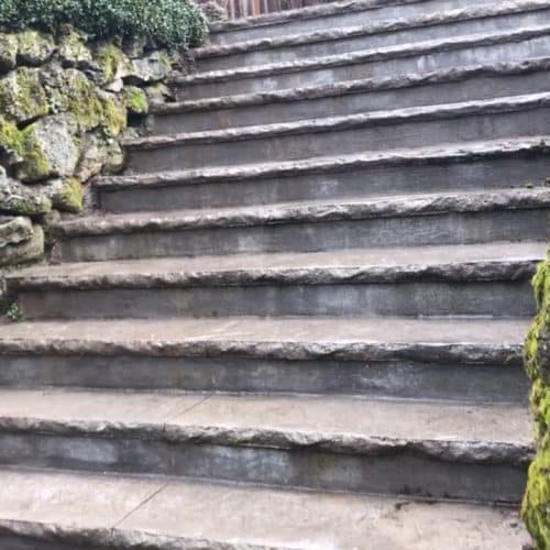 A mossy rock wall flanks newly poured steps up to a home